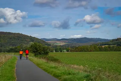 Two cyclists on a rural path between green fields and hills